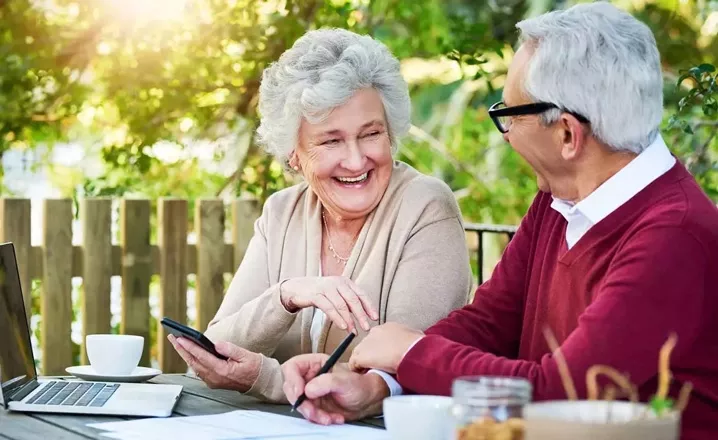  A retirement-aged couple laughs together while they file their taxes outside on their porch.
