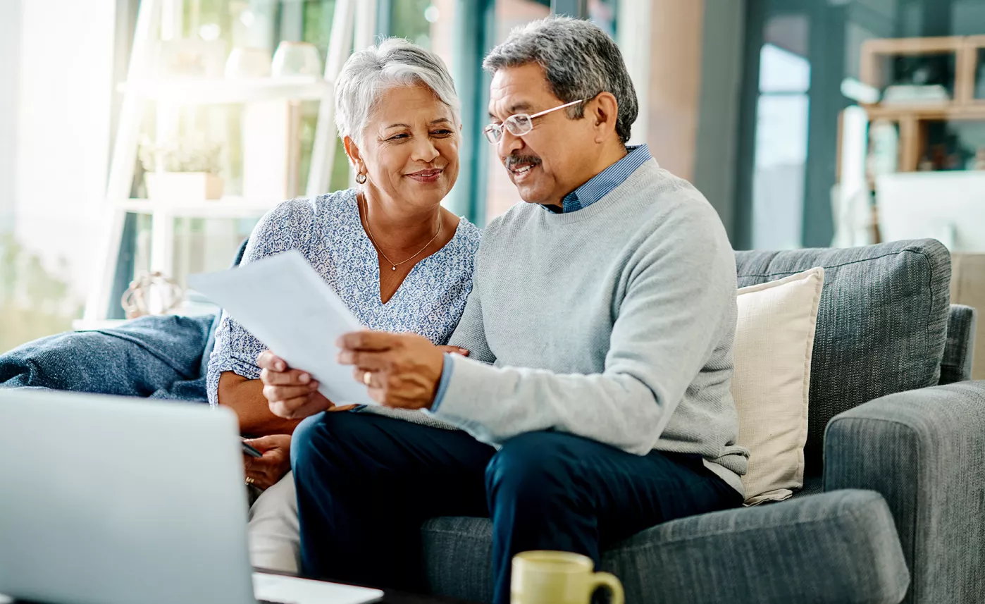  A retirement-aged couple read financial documents about stock options and retirement plans on the couch in their home.
