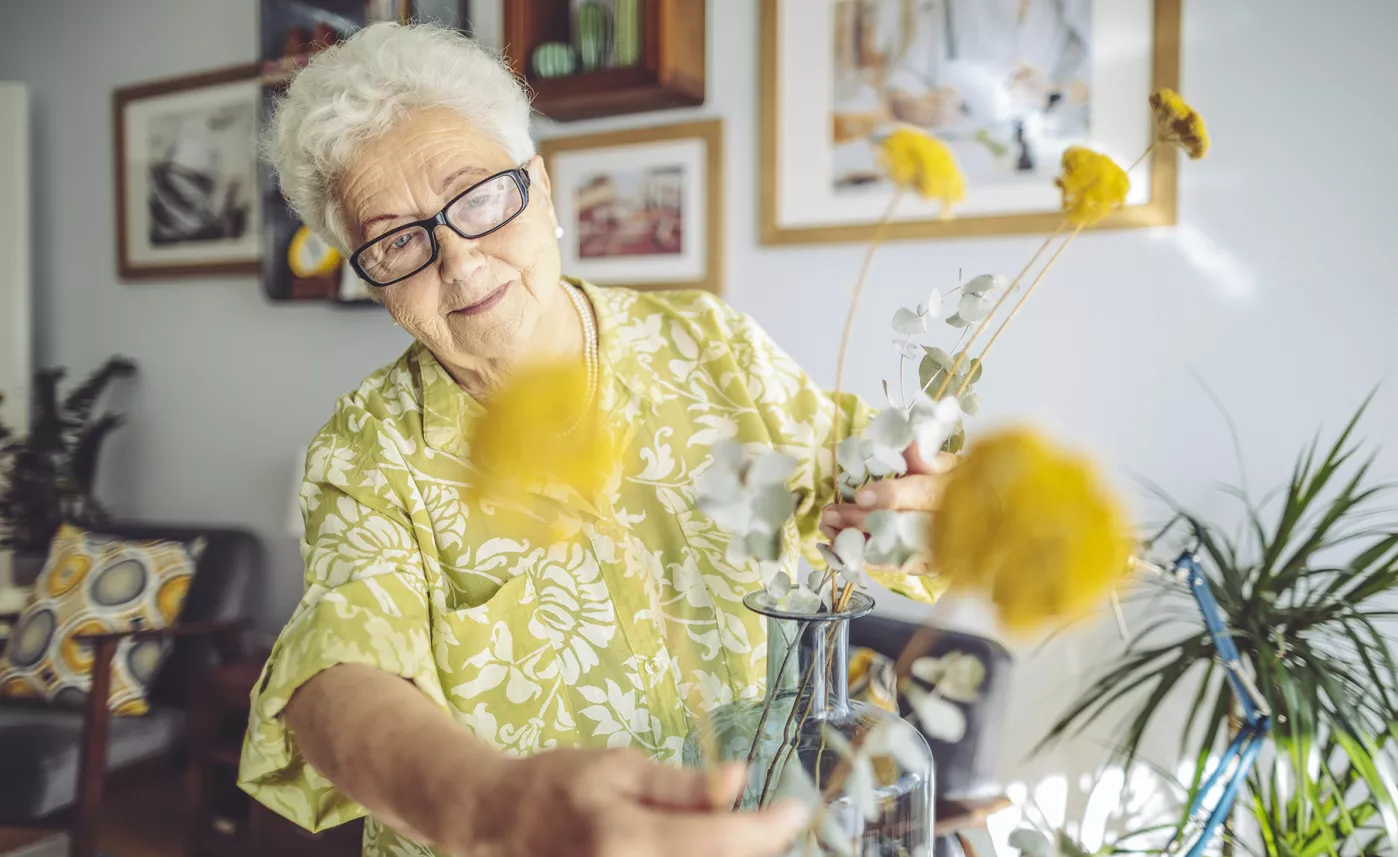  A retirement-aged woman puts together a flower arrangement in her home.
