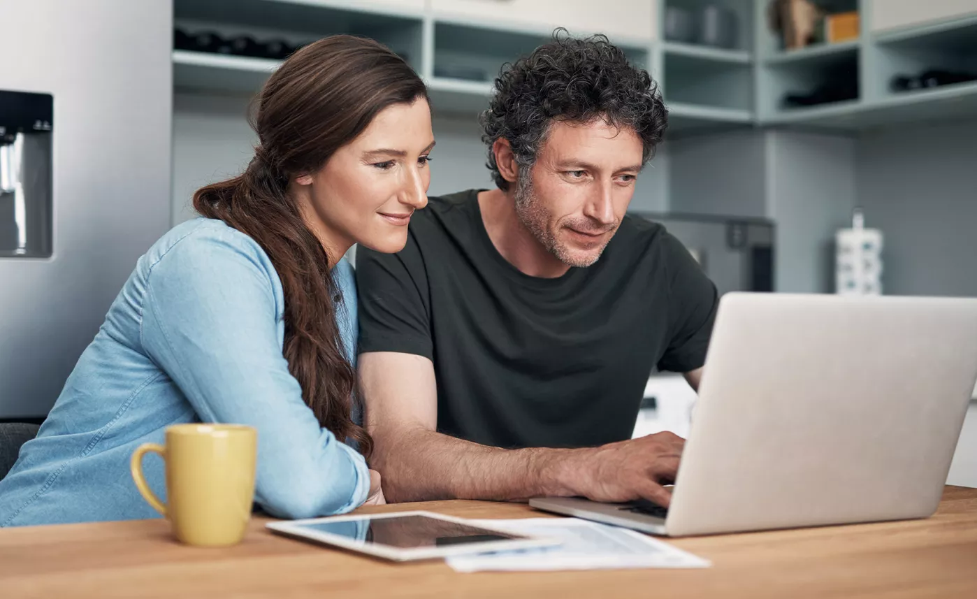  A couple sits at their kitchen table and reads about financial terms on their laptop.

