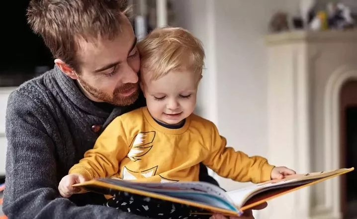  A young father reads from a picture book with his toddler son.
