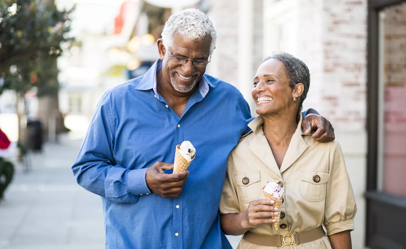  A retirement-aged couple smile and walk down the street with ice cream cones.

