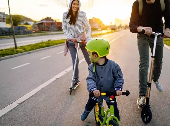  Man, woman and toddler riding scooters and balance bike.
