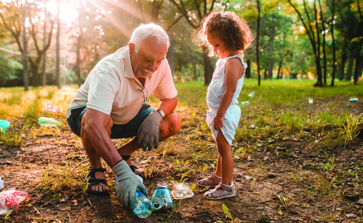  A grandfather helps his young granddaughter pick up trash in a park.

