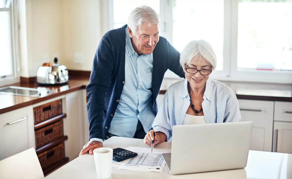  A retirement-aged couple check their retirement account on their laptop in their kitchen.
