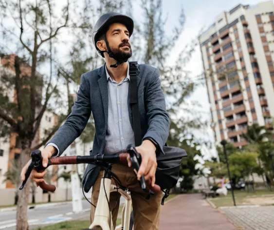  A man with a beard, wearing a helmet and suit, stands with his bicycle and looks up to his right.
