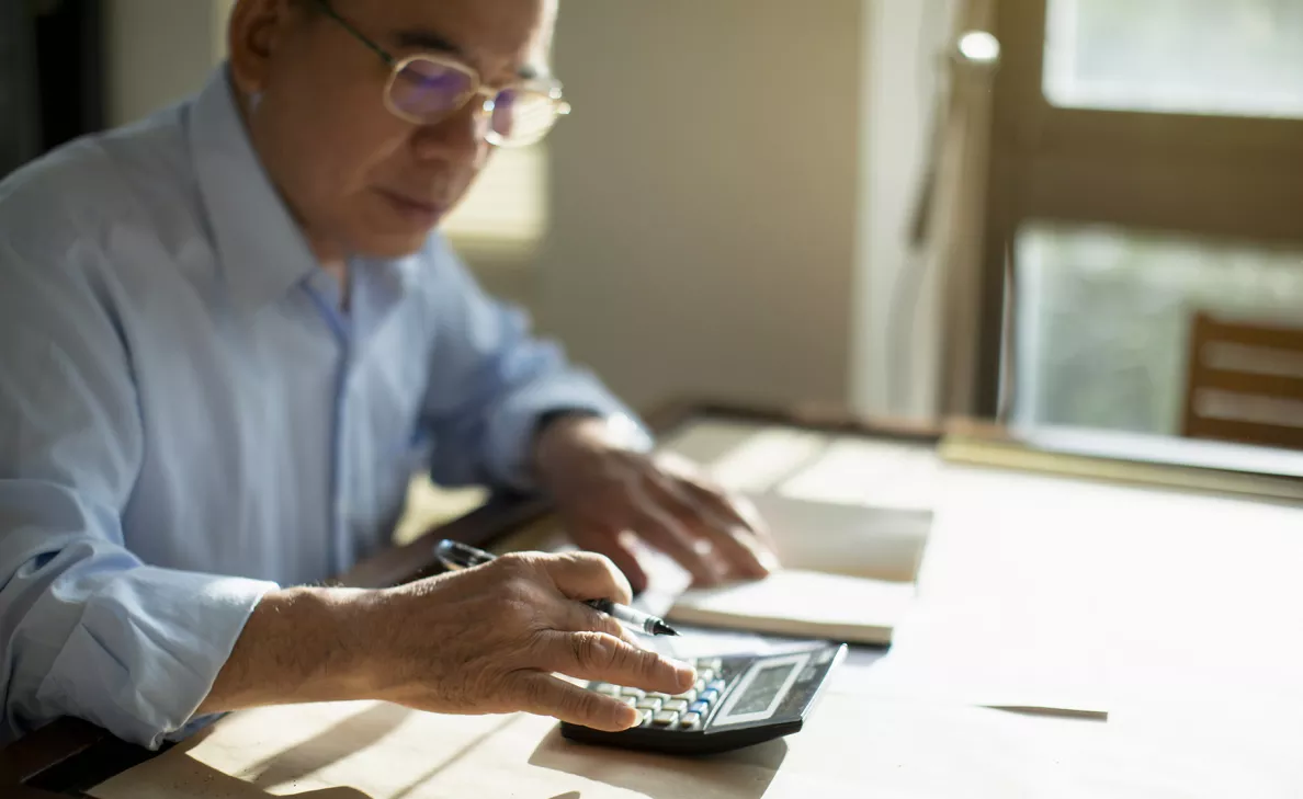 A retirement-aged Edward Jones client checks figures on a calculator at his desk.