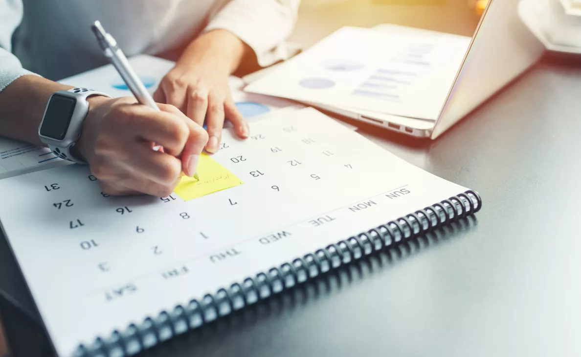 A person writes on a sticky note on a calendar.