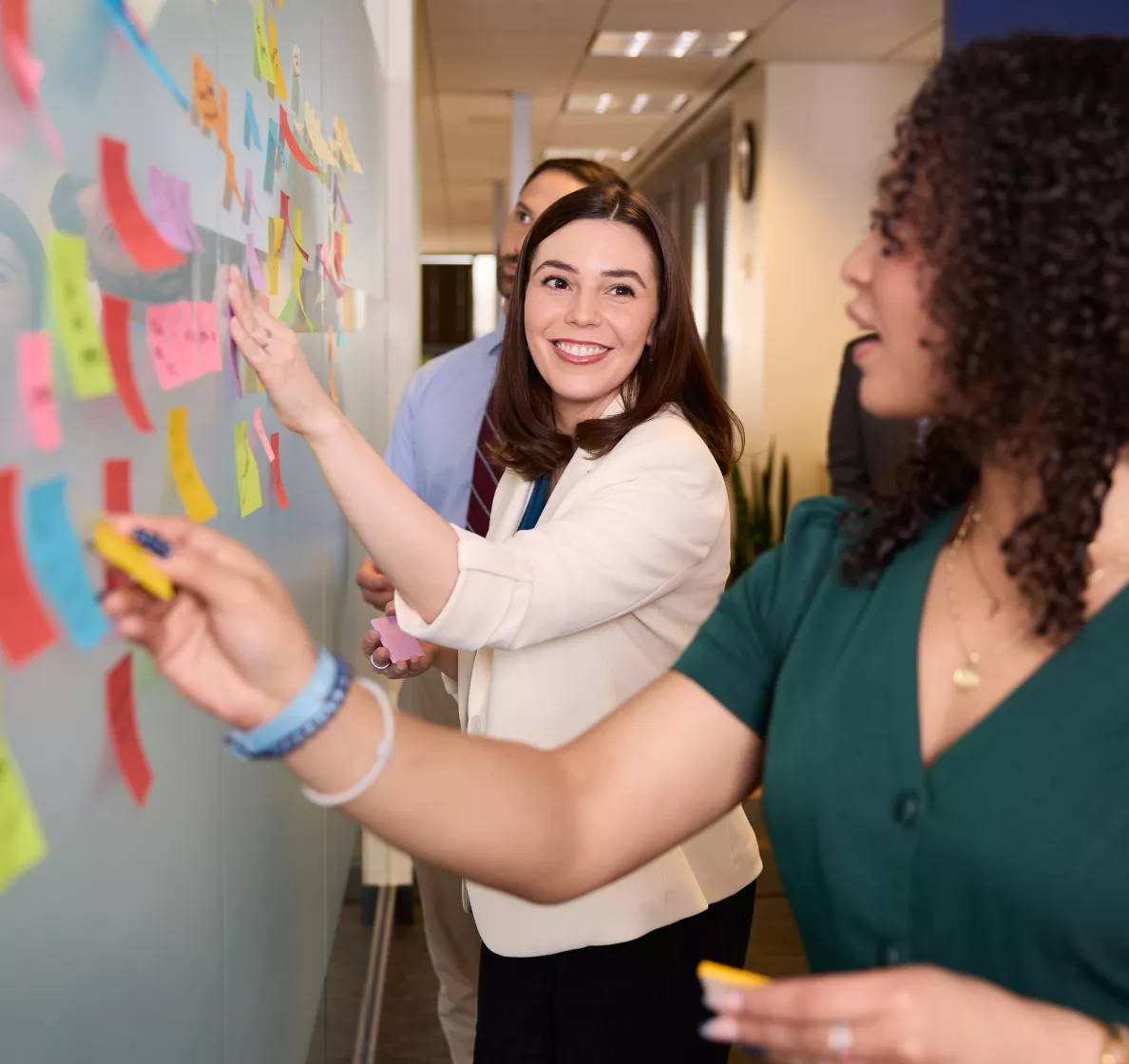  People placing colorful sticky notes on a wall during a collaborative workshop.
