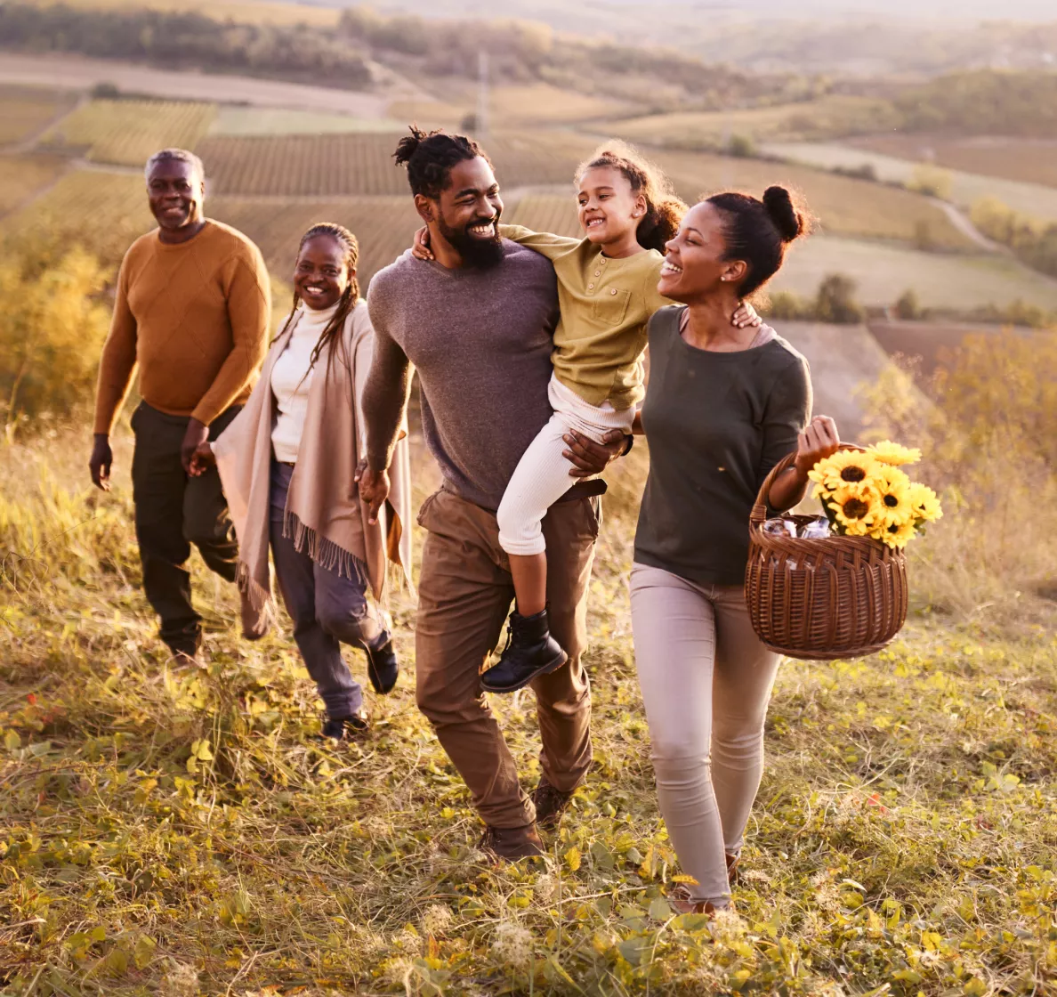  A group of people walking up a grassy hillside at sunset, with fields and rolling hills in the background.
