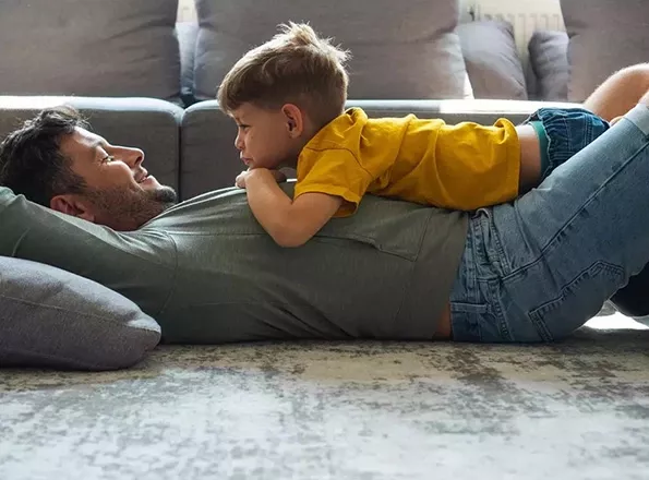 A young child lies on his father in the living room of their home.