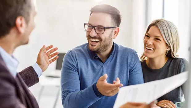 Two people smile and point to a paper while looking at another person Two people smile and point to a paper while looking at another person