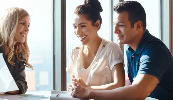 A smiling couple sits with a businesswoman at a desk A smiling couple sits with a businesswoman at a desk