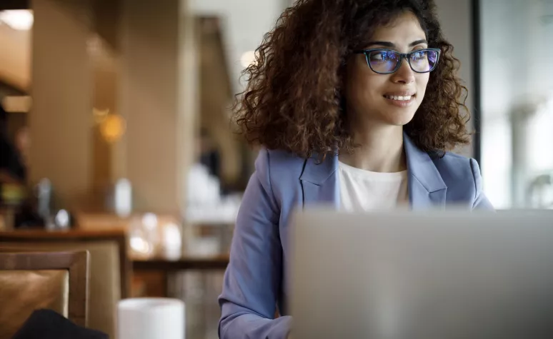 A professional woman looks at her open laptop in a cafe with a cup of coffee next to her. A professional woman looks at her open laptop in a cafe with a cup of coffee next to her.