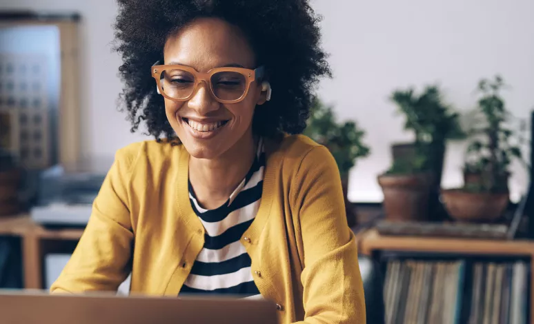 A woman smiles as she pays bills on her laptop in her home office. A woman smiles as she pays bills on her laptop in her home office.