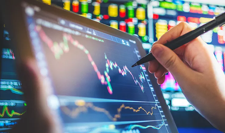 Hand using a stylus on a tablet displaying stock market charts.