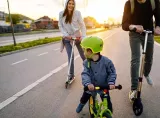 Man, woman and toddler riding scooters and balance bike.