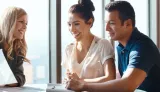 A smiling couple sits with a businesswoman at a desk