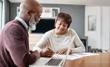 A couple looks over documents with financial information with their laptop open.