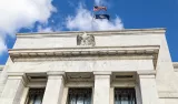 Federal Reserve building facade with U.S. flags against a blue sky.
